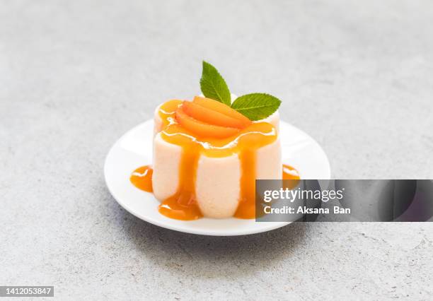 vegan dessert. apricot pudding, panna cotta with topping, decorated with slices of fruit and apricot jelly in the shape of pearls, on a plate. light grey background. top view - panna cotta photos et images de collection