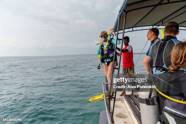 a woman - diver wearing a diving suit and aqualung, is preparing to jump to the ocean from a boat. - aqualung diving equipment stockfoto's en -beelden