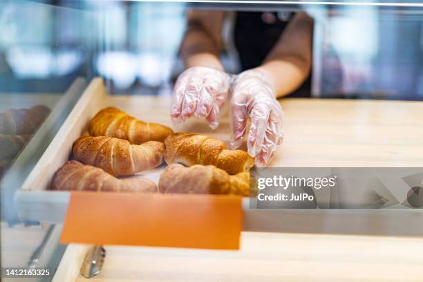 hand mit handschuhen ein französisches croissant vom tablett an der verkaufstheke nehmen - cake sale stock-fotos und bilder