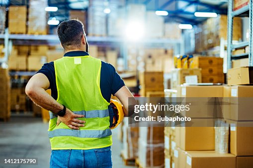 A warehouse worker having back pain and rubbing it. A warehouse worker having back pain and rubbing it.
