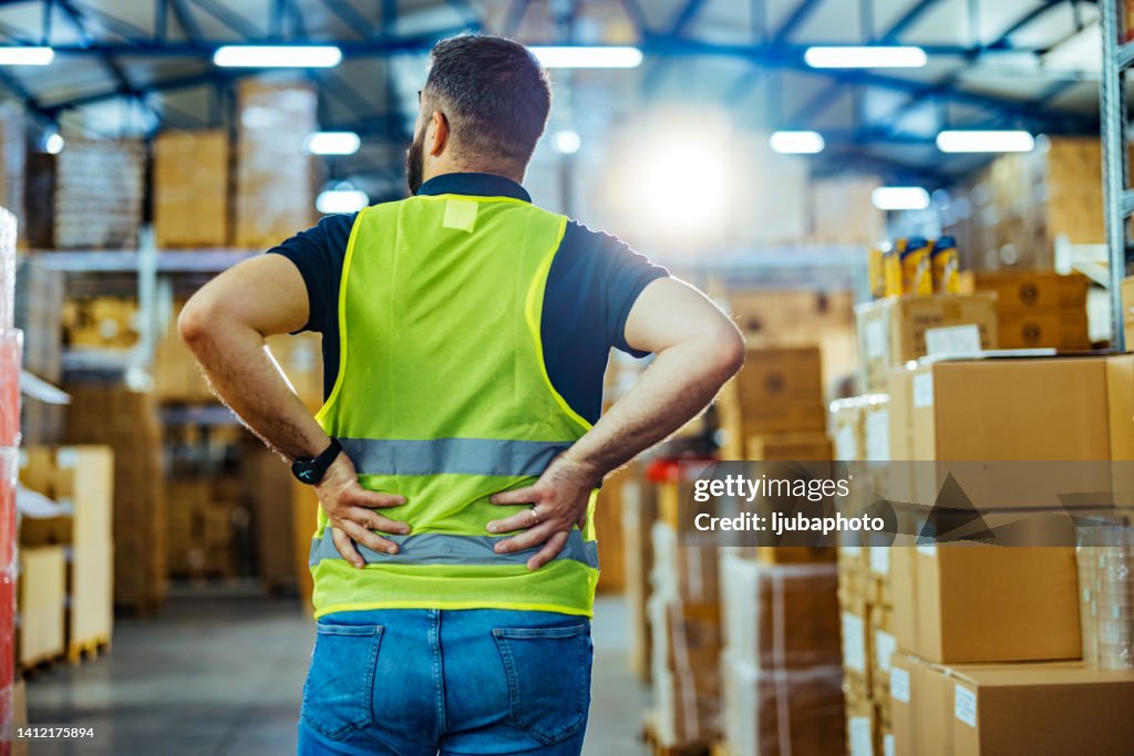 Rear view of male warehouse worker having back pain from hard work