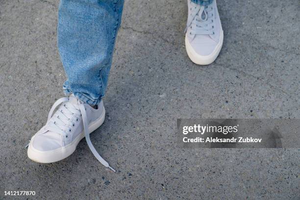 the girl's legs are in new clean modern sneakers and jeans, one lace is untied. a woman in sports shoes walks on the sidewalk or asphalt. fashionable and stylish lifestyle. the concept of an active lifestyle, hiking. daily walking for health. - feet girl stock pictures, royalty-free photos & images