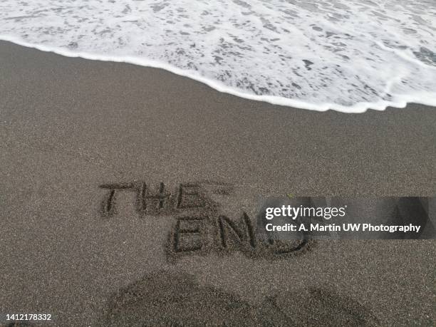 the end message written on the sand, on the shore of a beach with a wave coming and about to erase it. - beenden stock-fotos und bilder