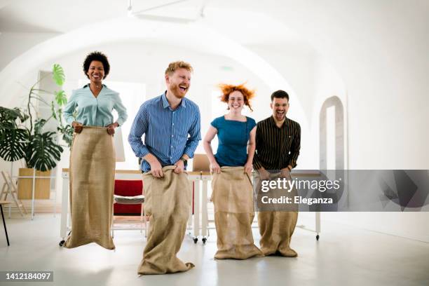 group of happy entrepreneurs having fun on a sack race in the office - sack race stock pictures, royalty-free photos & images