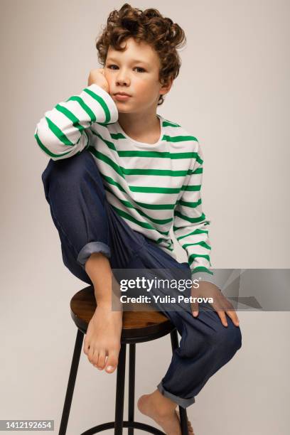 portrait of a curly-haired boy in a vest and jeans on a white background in the studio - kids fashion stockfoto's en -beelden