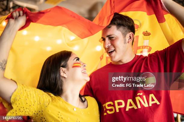 couple watching a soccer game and celebrating with a spanish flag - national day of spain stock pictures, royalty-free photos & images
