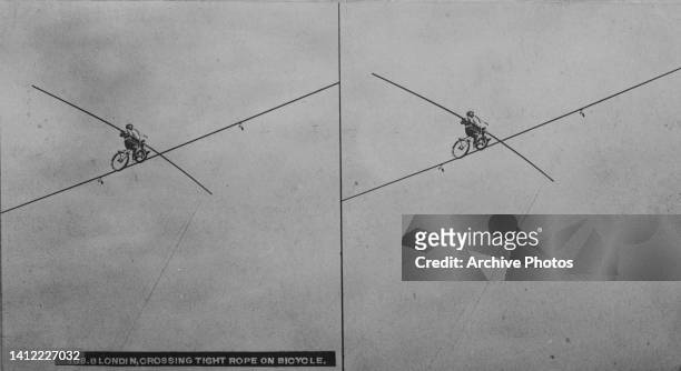 Stereoscopic image showing an tightrope walker crossing a highwire on a bicycle with the aid of a balancing pole, United States, circa 1895. Despite...