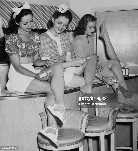 Mary Allen Gould, Doris Poland, and Ellen Shalit , three local models, apply stick 'stockings' being offered at Helena Rubinstein's Bare-Leg Bar....