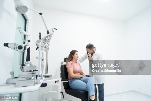 woman sitting during eye exam next to ophthalmologist - phoroptor stock pictures, royalty-free photos & images