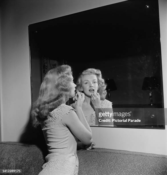 American actress Marilyn Monroe uses a mirror to apply lipstick at a 'dream house' - a competition prize, which she is presenting to the winner in...