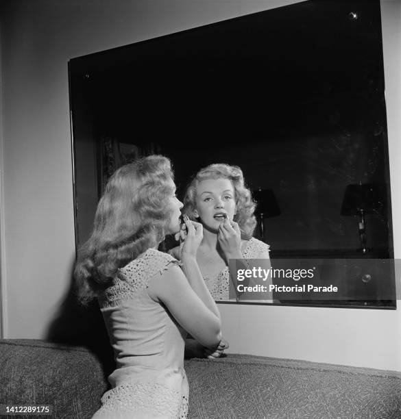 American actress Marilyn Monroe uses a mirror to apply lipstick at a 'dream house' - a competition prize, which she is presenting to the winner in...