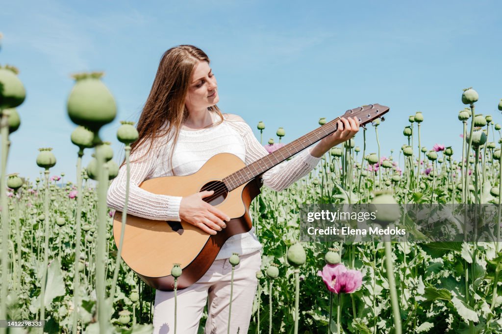 A charming young girl plays the guitar in a field of purple poppies on a bright sunny day.