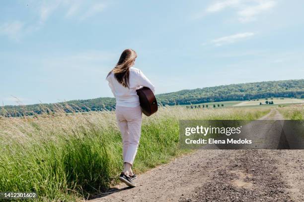 a girl with an acoustic guitar walks along a country road in summer - escritor de canções imagens e fotografias de stock
