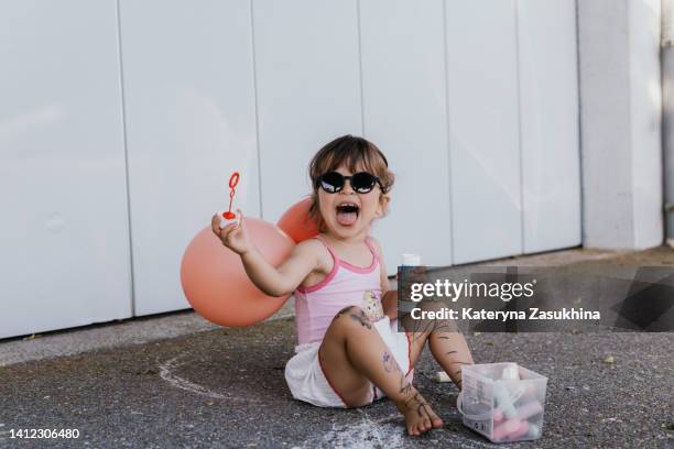 an adorable toddler girl playing with bubbles outside - innocence fotografías e imágenes de stock