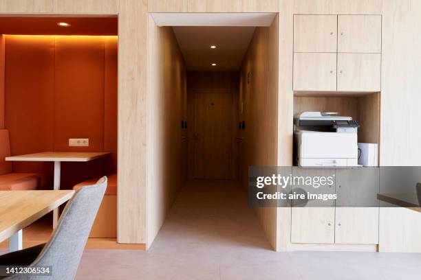 corridor leading to exit door of modern office with bookshelves printer paper tables and chairs - glowing doorway stock pictures, royalty-free photos & images