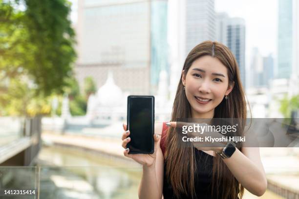 asian woman pointing at a smart phone in the city - sim card photos et images de collection