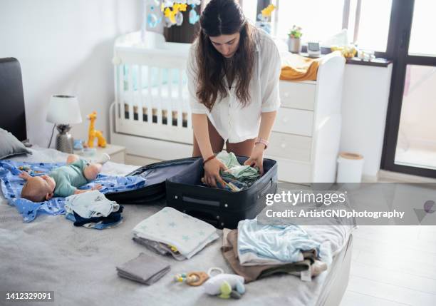 mother packing baby clothing in a suitcase. - baby bag bildbanksfoton och bilder