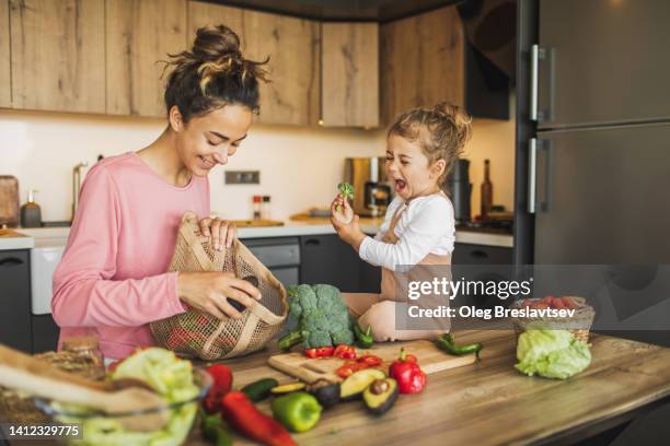 mother and daughter preparing fresh vegetables for cooking at kitchen. both laughing - preparación de alimentos fotografías e imágenes de stock