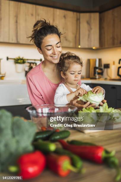 mother with daughter cooking together at kitchen. making fresh salad with greens and organic farm vegetables - healthy family stock-fotos und bilder