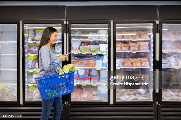 woman buying groceries at the supermarket and reading her shopping list - refrigerated section supermarket stock pictures, royalty-free photos & images