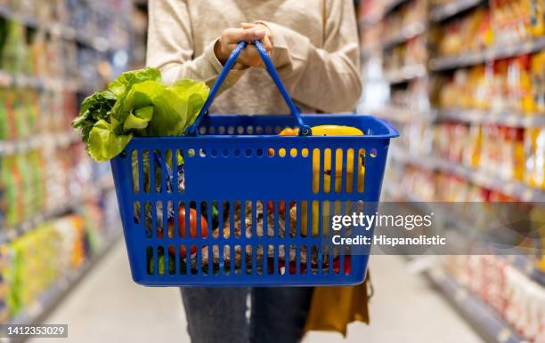 woman at the supermarket carrying a shopping basket - endast en medelålders kvinna bildbanksfoton och bilder