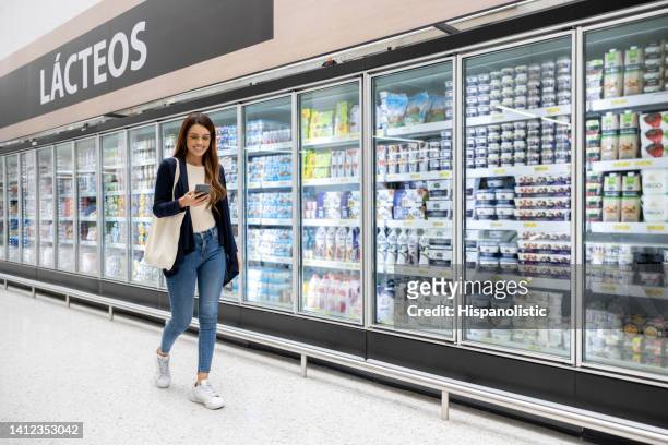 woman buying groceries at the supermarket following a shopping list - dairy aisle stock pictures, royalty-free photos & images