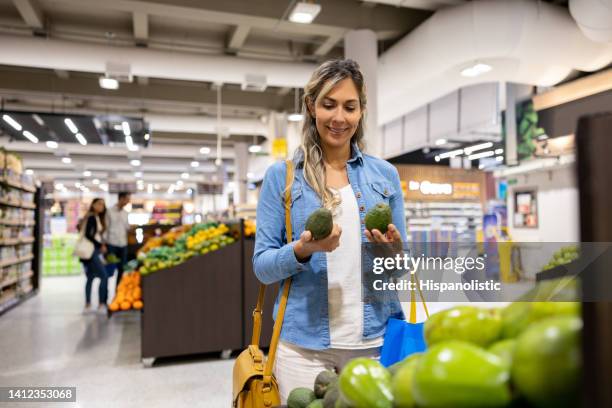 mujer feliz comprando aguacates en el supermercado - mid adult fotografías e imágenes de stock