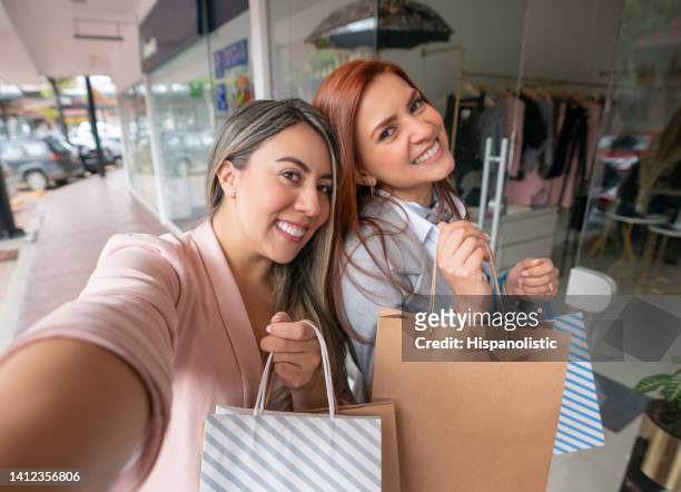 happy women taking a selfie while shopping at the mall - latin american and hispanic shopping bags stock pictures, royalty-free photos & images