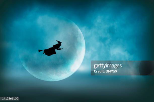 flying halloween witch silhouetted in front of large moon - heks stockfoto's en -beelden