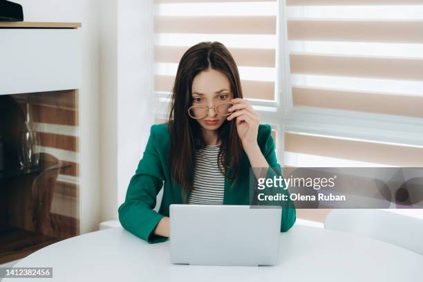 young woman taking off eyeglasses looking at laptop indoors. - striped blazer stock pictures, royalty-free photos & images
