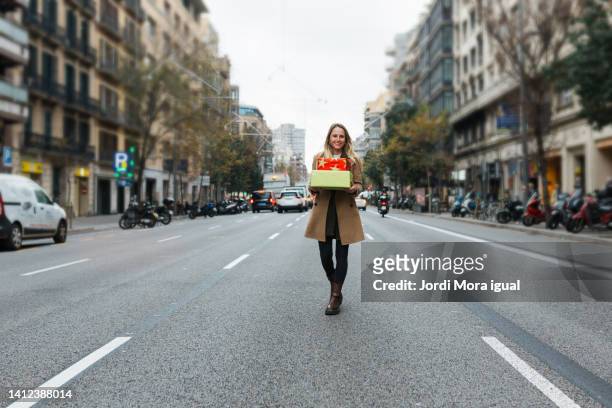 a cheerful woman holding christmas presents standing in the middle of a street. - barcelona day stock-fotos und bilder