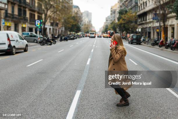 woman crossing the street while talking on a cell phone - clumsy walker stock pictures, royalty-free photos & images