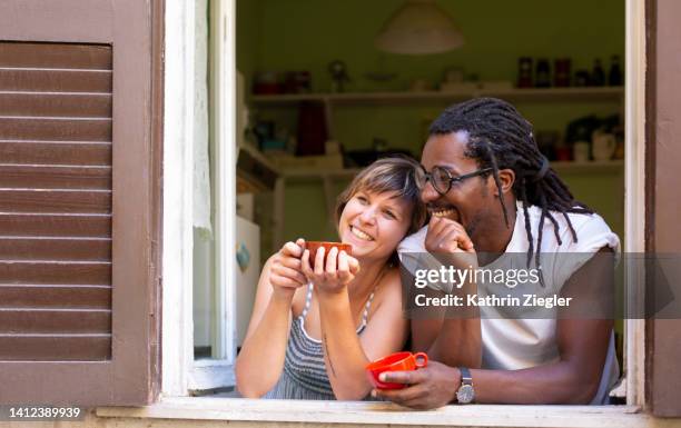 happy couple at open kitchen window, having a cup of coffee - café rouge photos et images de collection