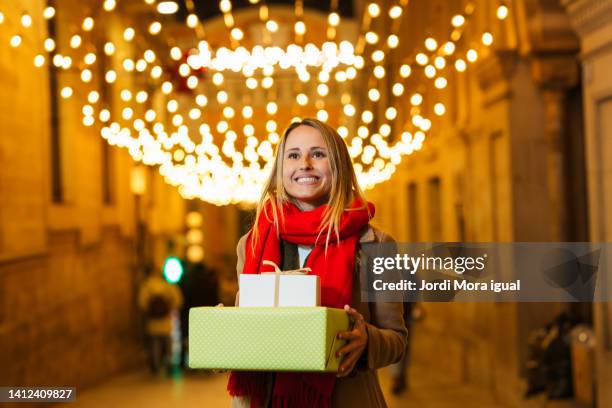 woman dressed in casual clothes walking with wrapped gifts along a city boulevard. - red grant stock pictures, royalty-free photos & images