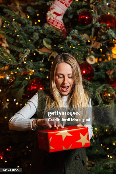 happy woman in casual clothes opens a magical christmas gift at home, in the background a christmas tree. - the red room opening party inside stock pictures, royalty-free photos & images