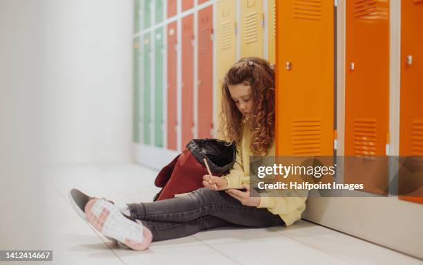 little sad girl sitting in school locker room, writing notes. - school locker room stock pictures, royalty-free photos & images