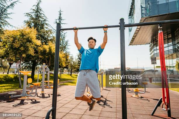 young man doing pull-ups on a bar outdoors - climbing frame stock pictures, royalty-free photos & images