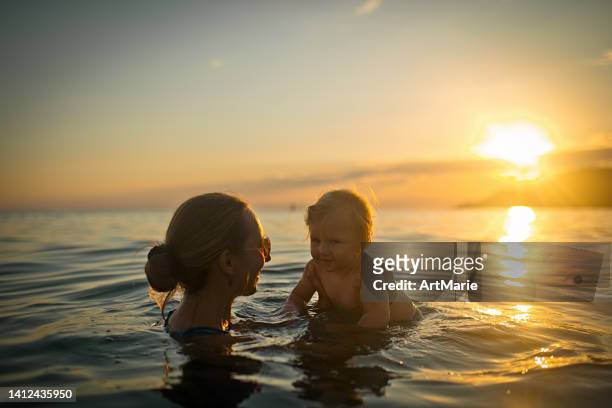 Baby girl with her mother enjoying sea in sunset
