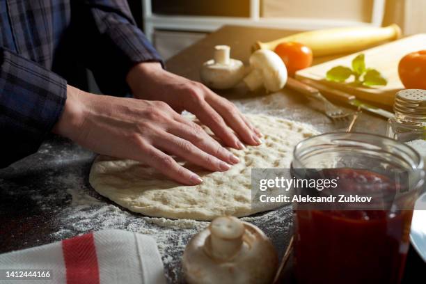cooking italian vegetarian pizza with vegetables and mushrooms at home, pizzeria or cafe. a woman baker, pastry chef or cook kneads and rolls the dough with her hands, in a bakery. the concept of food. step-by-step instructions, do it yourself. step 1. - woman cook foto e immagini stock