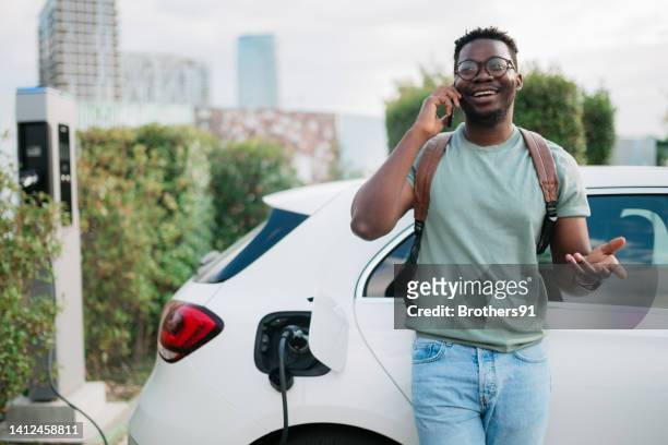 junger erwachsener mann, der sein elektroauto lädt - elektroauto mensch stock-fotos und bilder