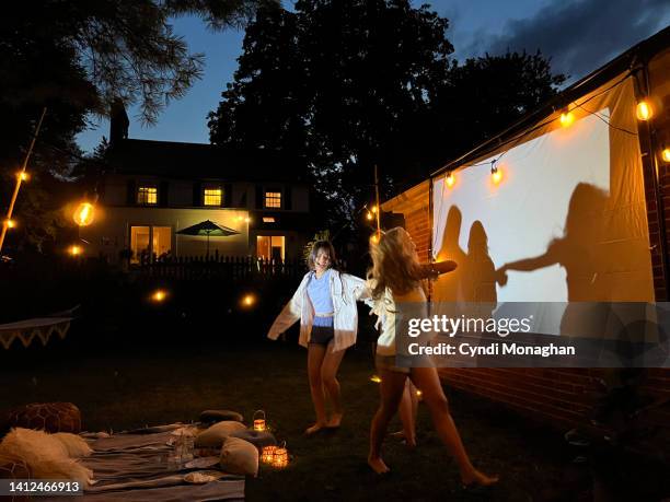 group of teenagers dancing in front of a glowing screen for outdoor movies - children dancing outside stockfoto's en -beelden