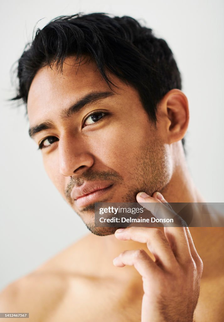 Skincare routine, skin and grooming done by a man against a white studio background. Portrait of one Asian male with soft, silky and smooth facial skin showing, touching and looking at his beard