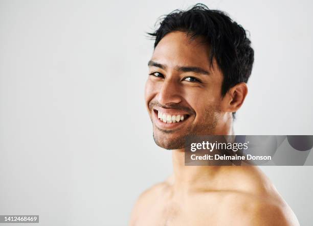 happy, smiling and cheerful man showing off his perfect white teeth and bright smile while standing against a studio background. portrait of the face of a young and joyful man showing his clear skin - asian man white background stock pictures, royalty-free photos & images