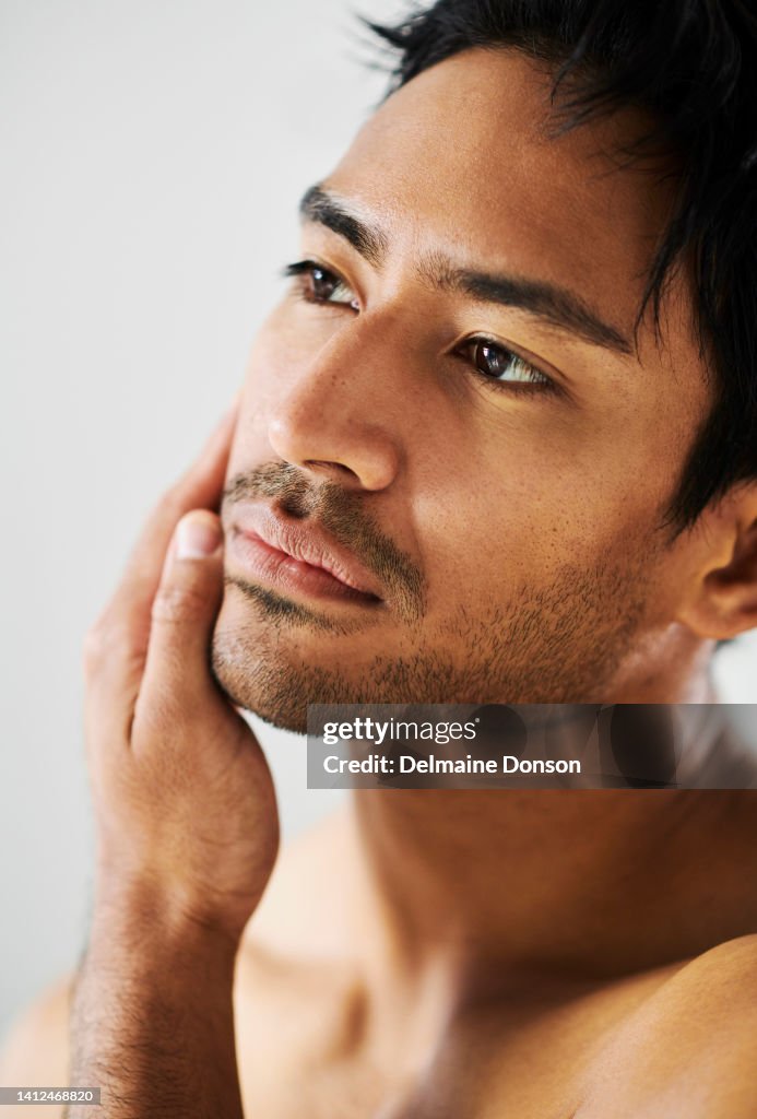 Close up of attractive young Indian male with stubble touching face and looking at skin. Metrosexual man examining complexion. The results of a good facial skincare or shaving regime