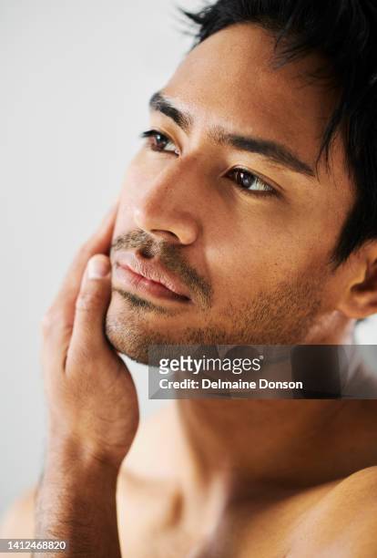 close up of attractive young indian male with stubble touching face and looking at skin. metrosexual man examining complexion. the results of a good facial skincare or shaving regime - man looking up beard chin imagens e fotografias de stock