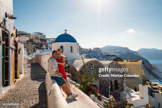 young adult couple sitting in santorini, greece - greece holiday foto e immagini stock