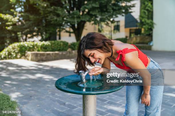 a young girl drinking water from a public drinking fountain in the park - hands fountain water stock-fotos und bilder