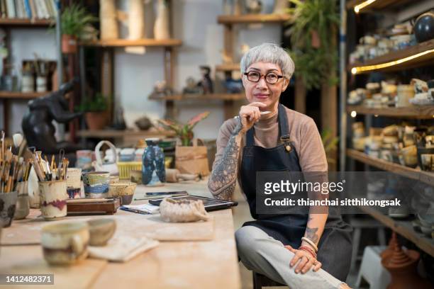 portrait female potter sitting in her studio. - women entrepreneur imagens e fotografias de stock