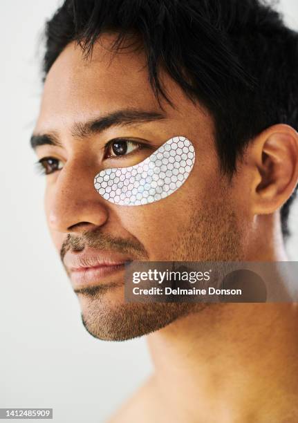 gel under eye patches for skincare on handsome male. face of a man serious about taking care of his skin while using a collagen beauty mask product to clear up dark circles and reduce puffiness - man eye cream imagens e fotografias de stock