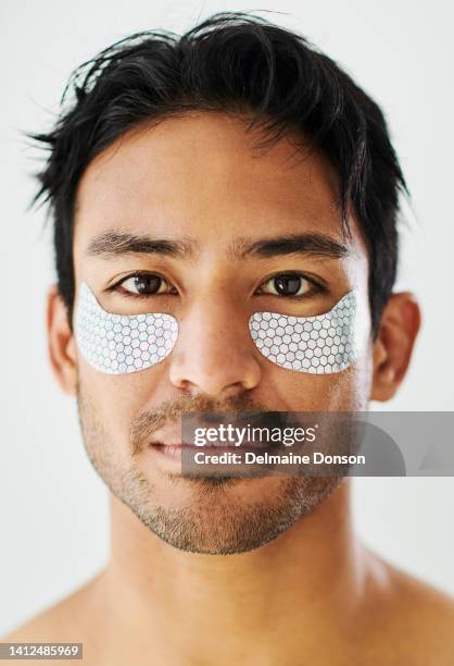 man hydrating his skin with under eye patches during a skincare and grooming routine against a grey background. portrait of a handsome young guy with healthy, glowing and flawless complexion - perfect complexion stock pictures, royalty-free photos & images